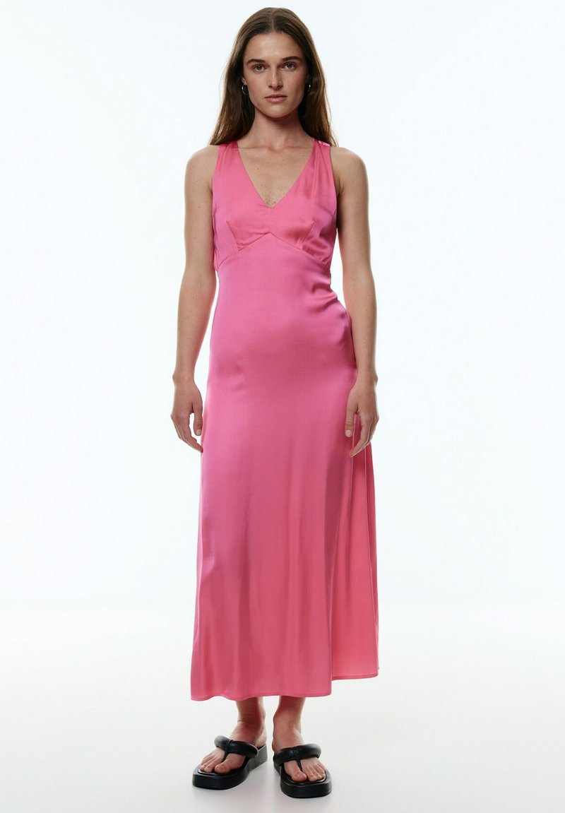 Rosa satin Maxi-Kleid mit V-Ausschnitt, tailliertem Oberteil und fließendem Rock. Das Model trägt schwarze Plateausandalen. Einfaches und elegantes Design.