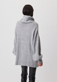 Przesadny szary sweter dzianinowy z dekoltem typu cowl, wzorem teksturowym i luźnymi rękawami, w parze z dopasowanymi czarnymi spodniami.