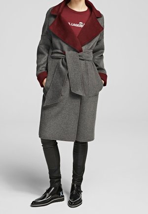 Person wearing a belted gray wool coat with burgundy wide collar and cuffs, black leather pants, and black leather ankle boots.