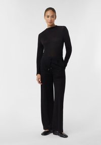 Top nero a maniche lunghe e pantaloni a gamba larga realizzati in tessuto morbido. L'outfit presenta un torso aderente e una vita regolabile con cordino per il massimo comfort.