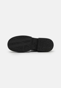 Soletta nera di scarpa da ginnastica con gomma testurizzata, caratterizzata da un motivo ondulato e un marchio in rilievo. Tacco arrotondato e design della intersuola flessibile.
