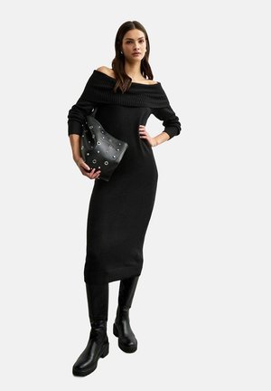 Svart off-shoulder stickad klänning med ribbad halsringning och långa ärmar, tillsammans med en svart väska med silverringdetaljer och knähöga stövlar.