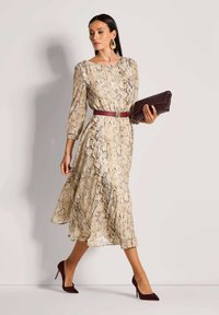 Beige Kleid mit Schlangenprint, dreiviertel Ärmel, tailliertem Bund und ausgestelltem Saum. Kombiniert mit einer burgunderfarbigen Clutch und passenden Absätzen.
