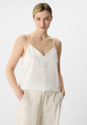 Weiße Satin-Camisole mit dünnen Spaghettiträgern und V-Ausschnitt, kombiniert mit beigen, hochgeschnittenen Hosen. Weiche, fließende Textur.