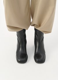 Botine din piele neagră la gleznă cu vârf pătrat și un design elegant. Fermeturele laterale și textura netedă le îmbunătățesc aspectul modern.