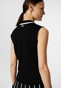 Black sleeveless knit top featuring a ribbed texture, white collar accents, and a logo at the back, with a fitted design and angled seams.