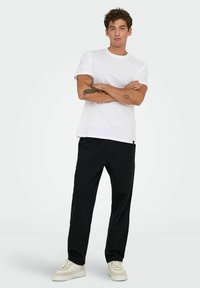 Hvid bomulds t-shirt, korte ærmer, rund hals. Sorte, løstsiddende bukser med to forlommer. Lette sneakers med et struktureret design.
