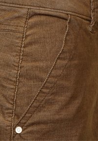 Tissu en velours côtelé marron avec des rainures verticales, comportant une poche latérale et un bouton en métal. Des coutures soignées mettent en valeur le design.