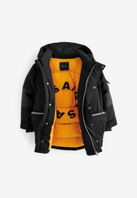 Chaqueta acolchada negra con capucha, que presenta un interior naranja brillante y letras negras. Incluye bolsillos con cremallera y cierres a presión.