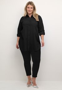 Camicia nera con bottoni, maniche lunghe, tasca sul petto e orlo curvo. Abbinata a jeans skinny neri e scarpe con tacco alto argento.