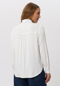 Witte blouse met lange mouwen en kraag, geplooid detail aan de achterkant en met knopen op de manchetten. Zachte stof met een gladde textuur. Casual pasvorm en afgeronde zoom.