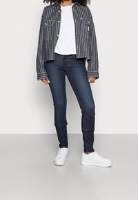 Dark blue denim skinny jeans paired with a black and white striped cropped jacket over a white t-shirt and white sneakers.