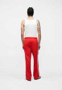 Rote Sporthose mit weißen Seitenstreifen, elastischem Bund und passendem Tanktop. Glatter Stoff, schmale Passform und flache Schuhe.