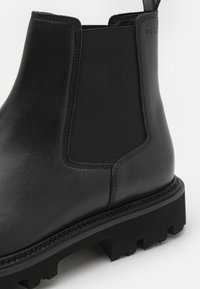 Mustmust mustripäevadega nahast Chelsea saapad elastse küljepaneeli, tõmbevahe ja mahuka tallaga ning peene reljeefse brändilogo ülaserval.