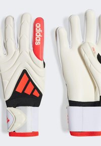 Guantes de portero Adidas, con material sintético blanco, detalles en negro, marca roja, dedos texturizados y una correa ajustable en la muñeca.