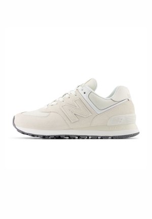 Jasnobeżowy sneaker New Balance z cholewką ze zamszu i siateczki, wiązany sznurowadłami, z amortyzowaną piętą i teksturowaną gumową podeszwą, widok z boku.