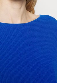 Blå ribbade tröja med en vid halsringning, mjuk textur och en kroppsnära design. Har vertikalt stickat mönster och en enfärgad nyans.