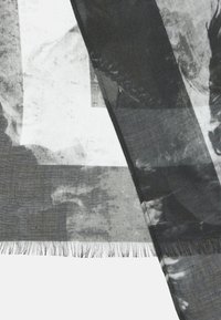Écharpe à motifs noir et blanc en tissu léger. Présente des bords frangés et des designs abstraits avec des tons et textures variés.