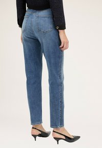 Jeans de mezclilla en azul medio con corte recto, que cuentan con dos bolsillos traseros y un panel lateral texturizado. Combinados con zapatos de tacón negros.