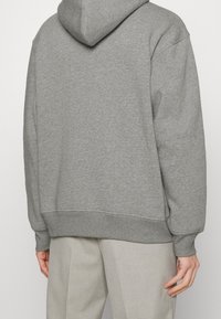 Sudadera con capucha gris de corte relajado, con tejido texturizado, puños y dobladillo acanalados, y un bolsillo tipo canguro que no es visible en esta vista trasera.