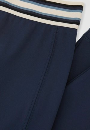 Marineblå træningsbukser med blødt, tekstureret stof og en elastisk taljebånd med flere striber i creme, lyseblå og sort.