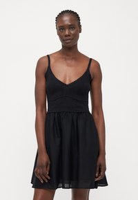Vestido negro con tirantes espagueti; cuerpo de punto con detalles texturizados, falda fluida. Tejido suave con un corte relajado.