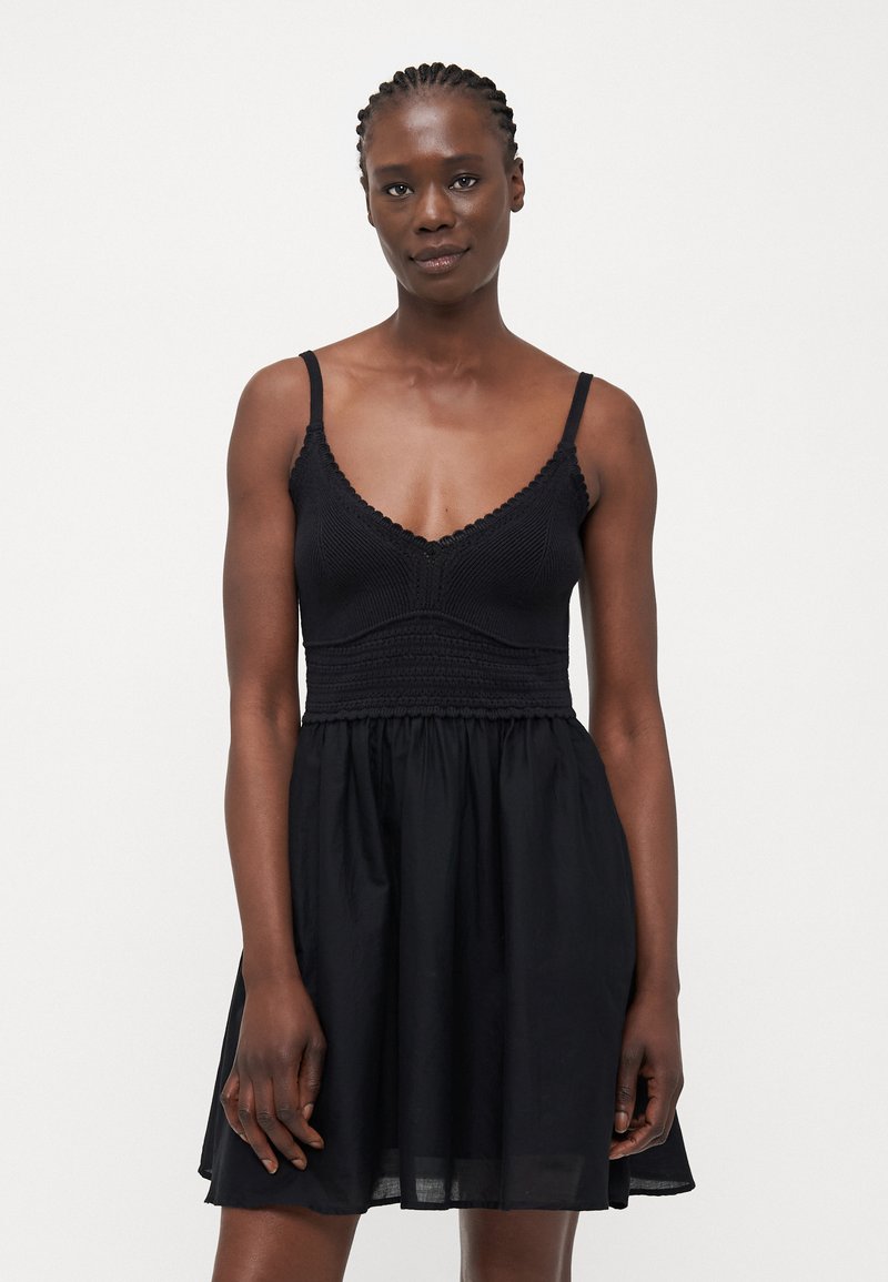 Vestido negro con tirantes espagueti; cuerpo de punto con detalles texturizados, falda fluida. Tejido suave con un corte relajado.
