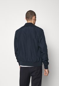 Námořnicky modrá bombera z lehkého materiálu, s žebrovaným límcem, manžetami a lemem. Hladká textura s minimem švů.