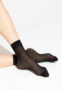 Chaussettes noires transparentes pour la cheville en matériau lisse, avec une bordure côtelée noire contrastante et une zone de pied renforcée.