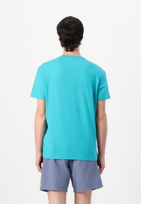 Turquoise T-shirt met korte mouwen van katoen, met een ronde hals en een lichte V-vorm aan de achterkant, gecombineerd met blauwe shorts.