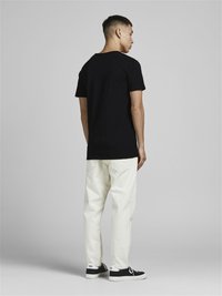 T-shirt en coton noir à manches courtes, associé à un pantalon beige clair et des baskets noires. Design simple avec une coupe décontractée.