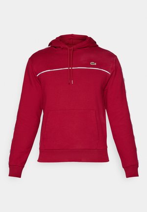 Rød hættetrøje lavet af bomuld med en front kangaroo lomme, hvid vandret stribe på tværs af brystet og logo på venstre side.