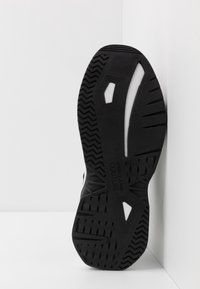 Black and white sneaker sole with textured tread patterns and "Versace Jeans Couture" branding visible on the bottom.