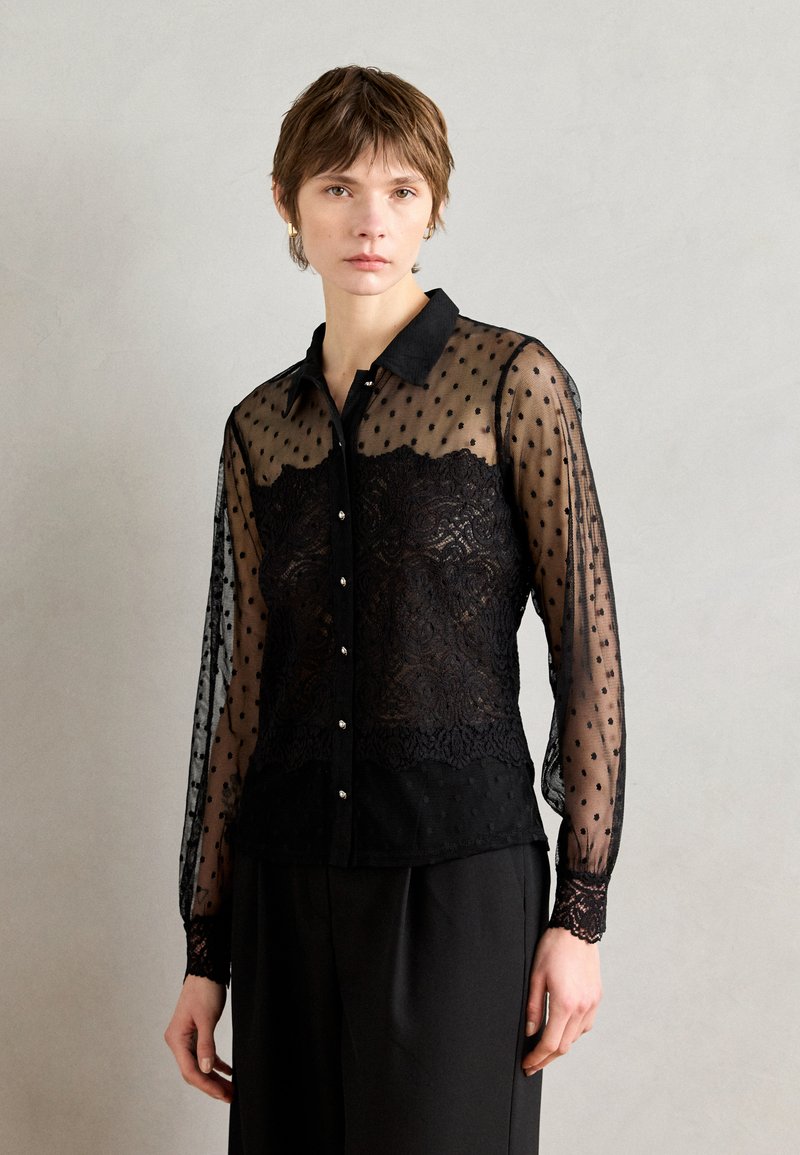 Blouse noire transparente avec motif à pois et détails en dentelle, dotée d'un col, d'une fermeture à boutons à l'avant et de manches longues avec poignets en dentelle.