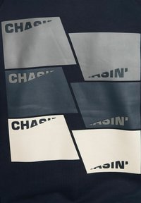 Felpa navy con molteplici stampe grafiche rettangolari in grigio e bianco, con la parola "CHASIN'" parzialmente visibile su alcune forme.