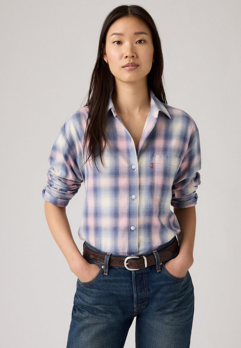 Lichtblauwe geruite overhemd met lange mouwen, met roze en witte accenten, met knopen aan de voorkant, opgerolde mouwen, gecombineerd met donkerblauwe jeans en een brownce riem.