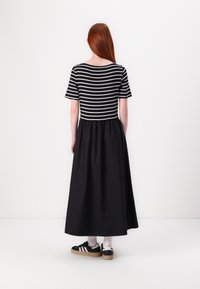 Svart maxi-kjole med stripet topp og ensfarget svart skjørt. Designet inkluderer korte ermer og en samlet midje. Svart sneakers er brukt.