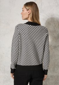 Maglione bianco e nero con un motivo geometrico a triangolo, colletto e polsini a coste neri e una vestibilità classica. Tessuto in maglia testurizzata.