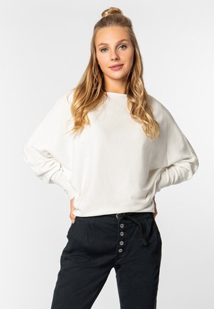 Weißes Langarmshirt mit lockerer Passform, runder Ausschnitt und gerippten Bündchen, kombiniert mit schwarzen Hosen mit Knopfverschluss und Zugband.