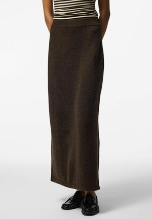 Femme portant une jupe en maille à taille haute, marron foncé, longueur cheville, associée à des mocassins noirs sans lacets et un haut rayé.