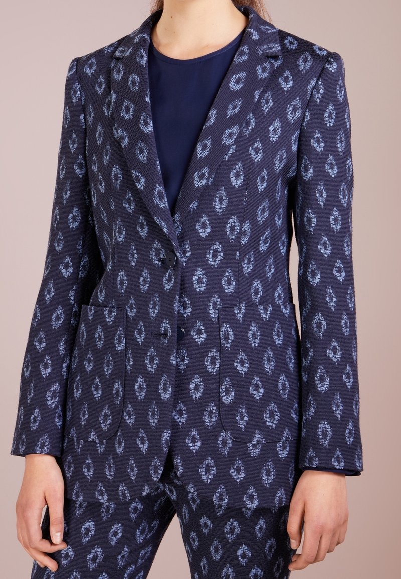 Mörkblå kavaj med blåmönstrad design, strukturerad form, slagkrage, två framfickor och enskild knappstängning.