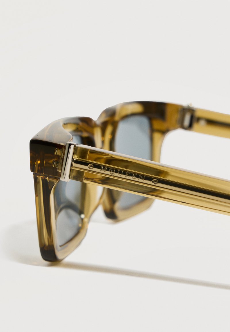 Brown translucent sunglasses with dark lenses, thick frames, and "MOUW" engraved on the gold-colored temple arm.