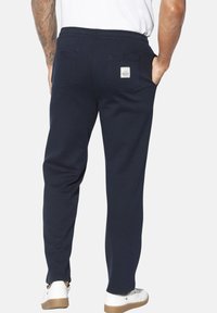 Marineblaue Sweatpants mit weicher Textur, elastischem Bund, zwei Gesäßtaschen und einem Markenpatch, kombiniert mit weißen Turnschuhen.