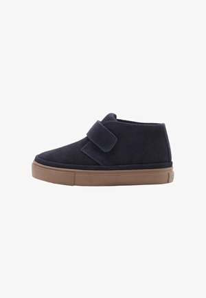 Scarpe alla caviglia in camoscio blu con punta arrotondata, dotate di una grande fascia a strappo e suola di gomma beige. Texture liscia con design semplice.