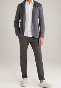 Blazer blu navy con texture e revers, indossato sopra una camicia bianca e abbinato a pantaloni grigio scuro e sneakers bianche.