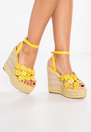 Yellow wedge sandals with floral accents, featuring a platform sole made of woven jute and a smooth, adjustable ankle strap.