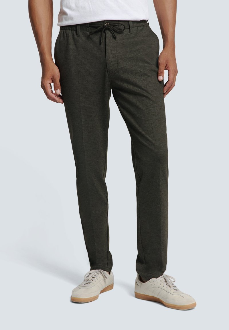 Dark green, lightweight jogger pants with an elastic drawstring waistband, side pockets, and a smooth texture. Worn with cream sneakers.