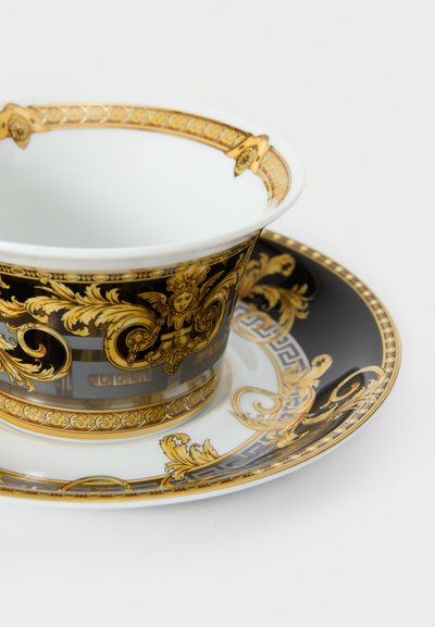 Porculanska šalica i tanjurić s detaljnim crnim i zlatnim uzorcima, koji sadrže cvjetne i ukrasne motive te glatku, sjajnu površinu.