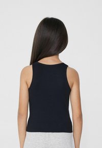 Zwarte geribbelde tanktop met brede schouderbanden, aansluitend ontwerp en rechte zoom, gedragen met lichtgrijze shorts. Eenvoudige en soepele structuur.