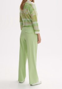 Zelený kostkovaný pletený svetr s krátkým střihem a dlouhými rukávy, doplněný světle zelenými kalhotami s vysokým pasem a zadní kapsou.